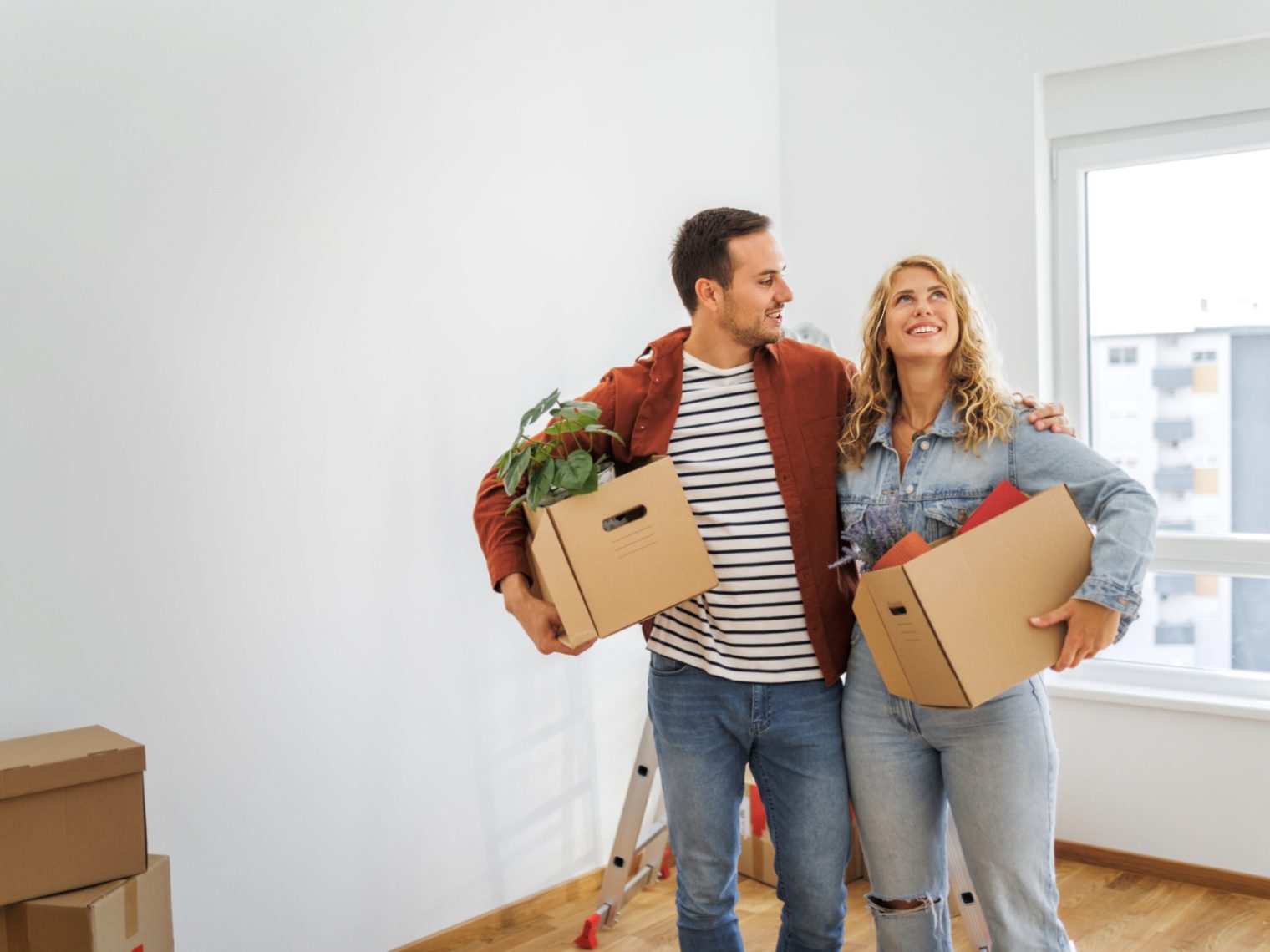 Couple holding moving boxes in the living room of a home.