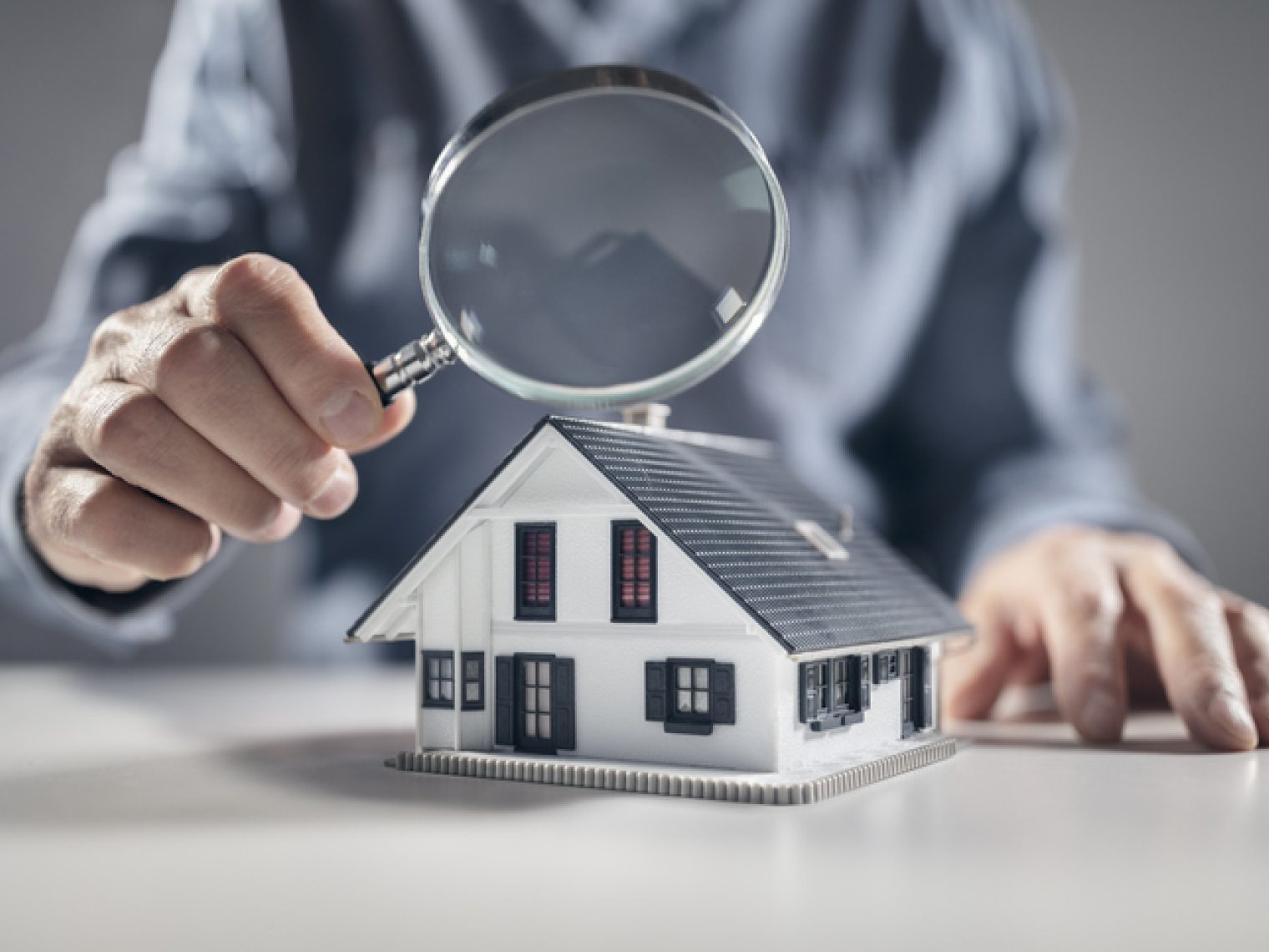 A person examines a model house with a magnifying glass.